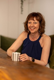 Gillian again enjoying her work holding a mug of tea and sat at a desk